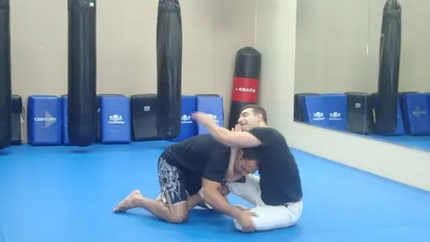 Felipe Soares drilling a guard-passing position with coach Keiser Girao on the blue mats at Minotauro BJJ, heavy bags hanging along the wall behind them.
