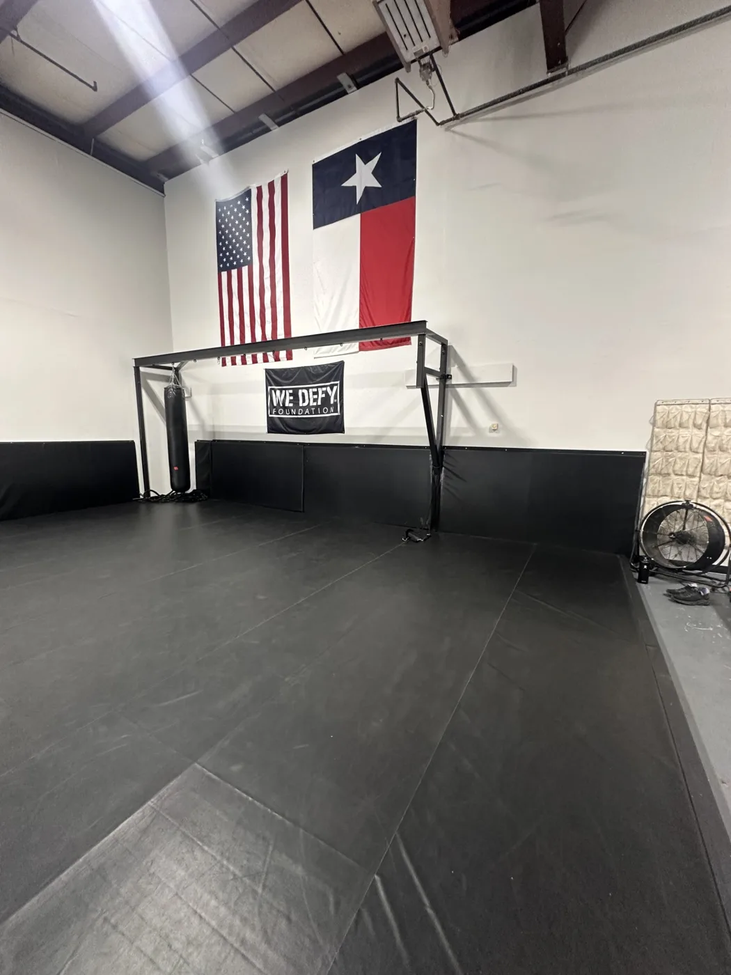 Wall-padded corner of the mat space with American and Texas flags and a heavy bag