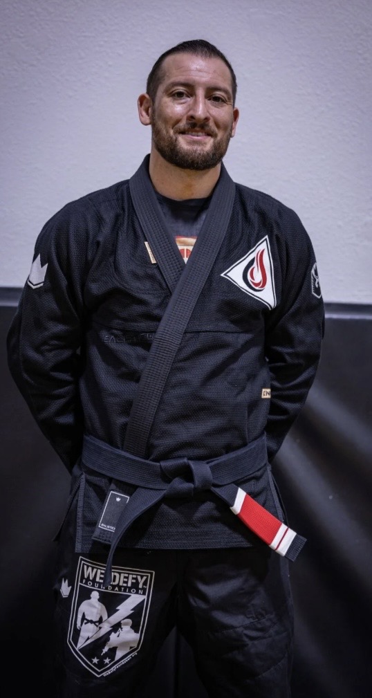 Professor Justin Wood, Lead Instructor for Train My Hands for War, standing in a black gi with his black belt tied at the waist.