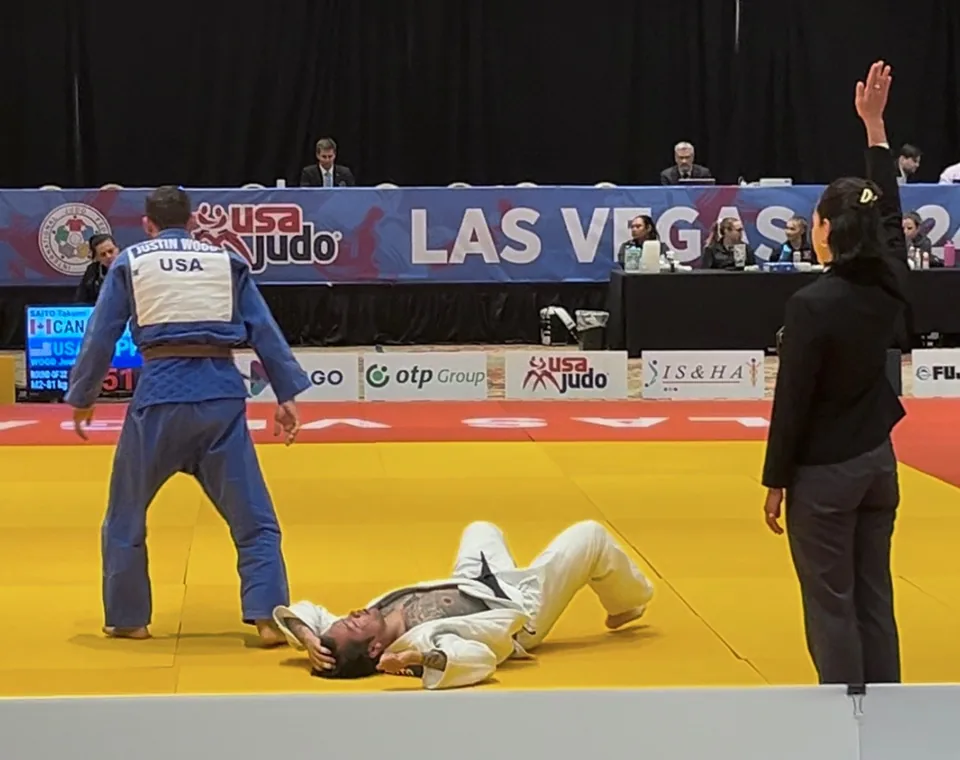 Justin Wood competing in a white judo gi at a USA Judo tournament in Las Vegas as the referee signals the score.