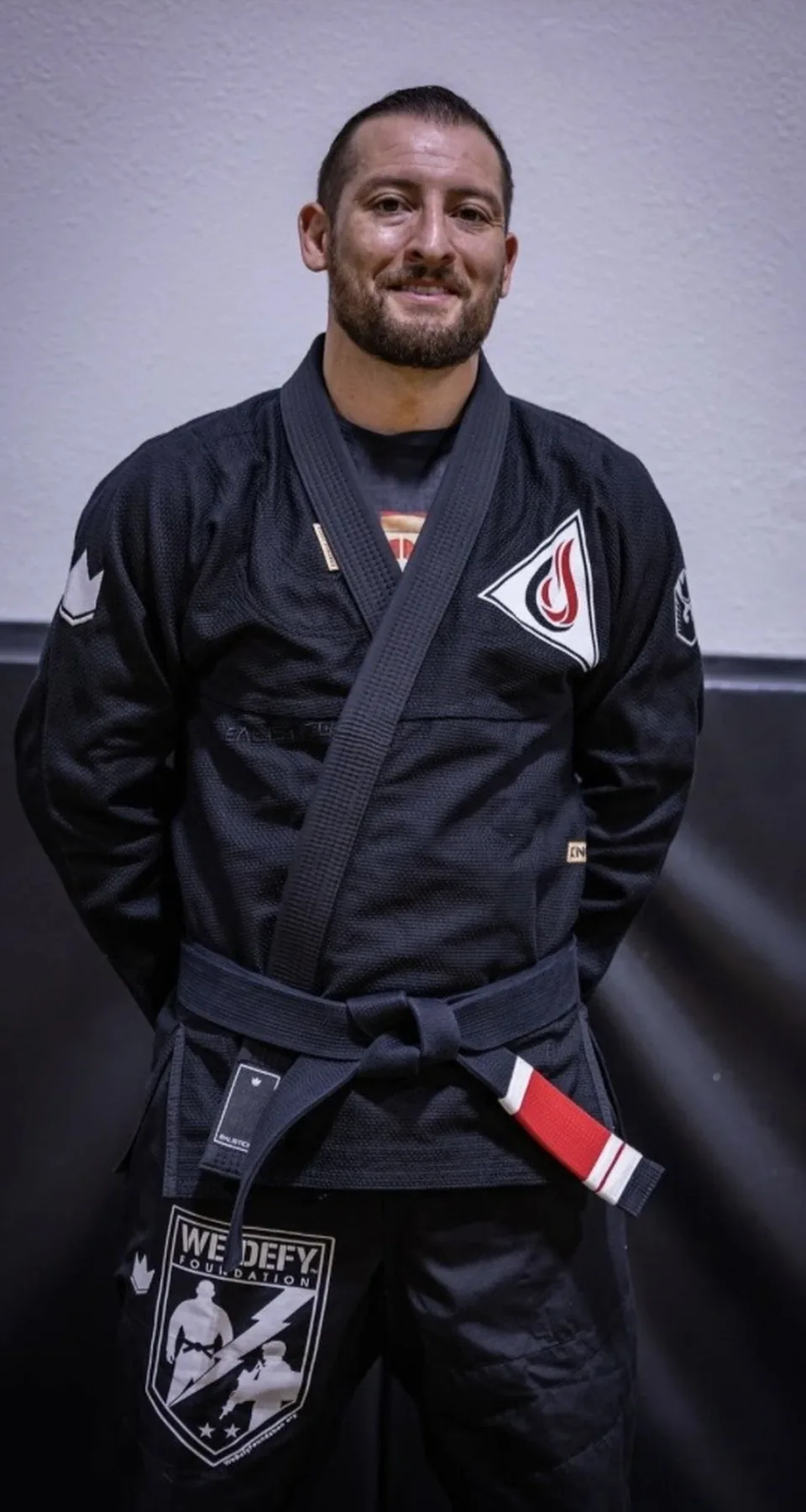 Professor Justin Wood, Lead Instructor for Train My Hands for War, standing in a black gi with his black belt tied at the waist.