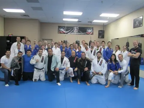 A large group of students and coaches in white and blue gis posed together on the blue mats at Team Minotauro Dallas, with Felipe Soares among the white belts.