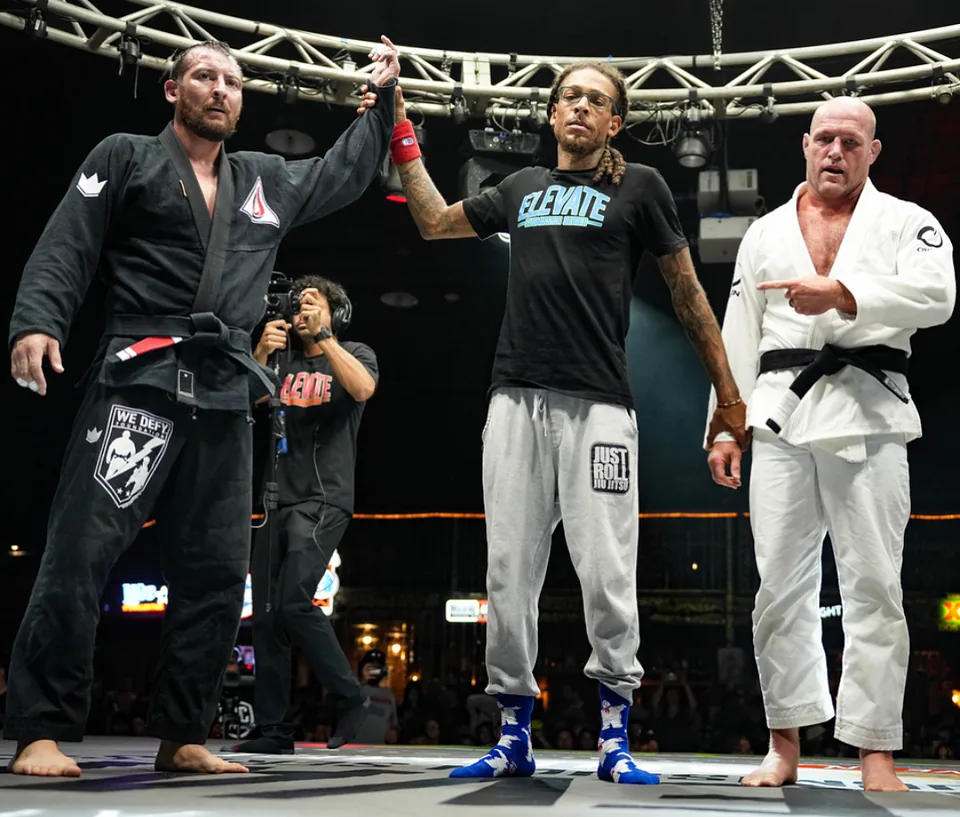 Justin Wood in a black gi having his hand raised by the referee after a black belt superfight win.