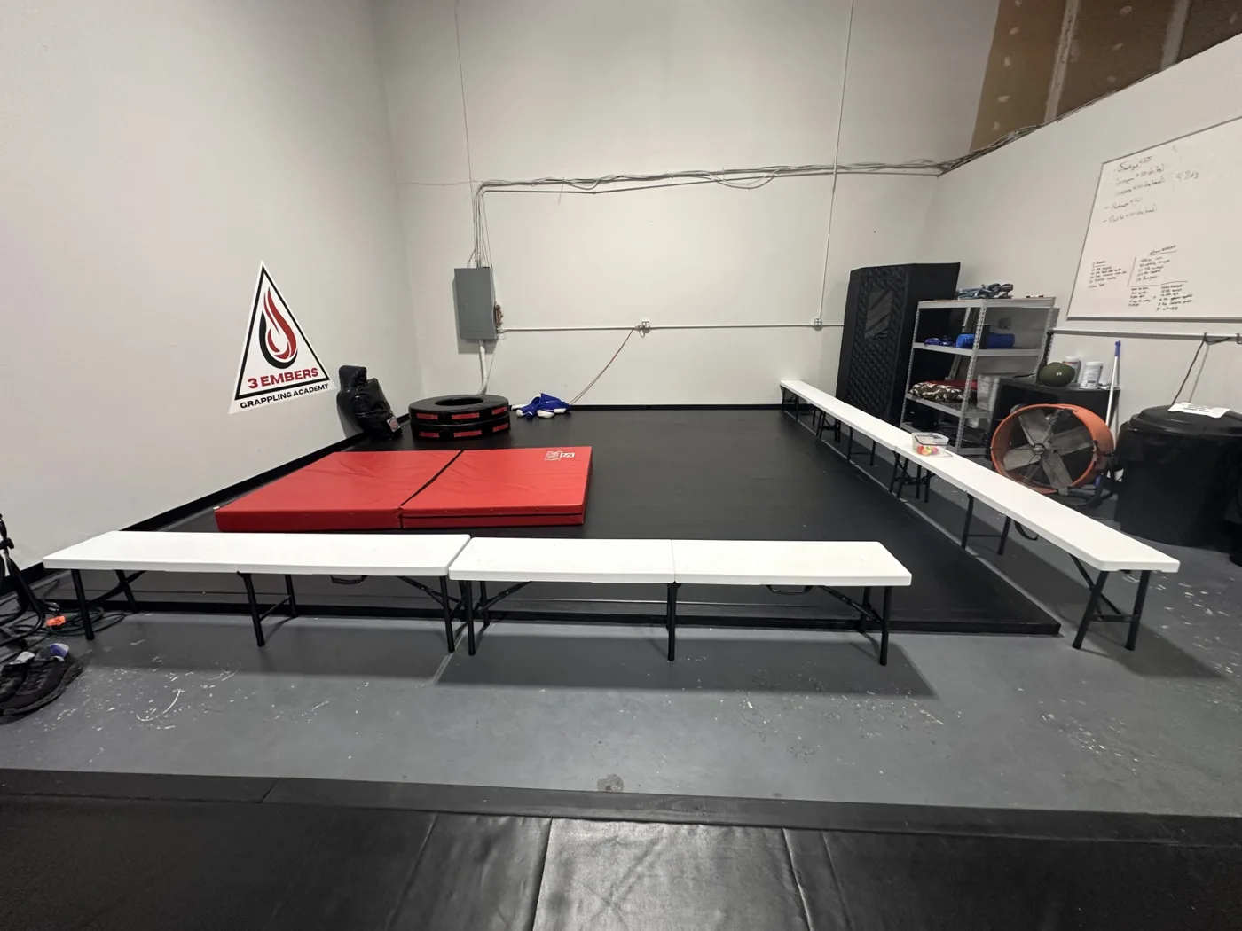 Mat area with the 3 Embers Grappling Academy banner and spectator seating