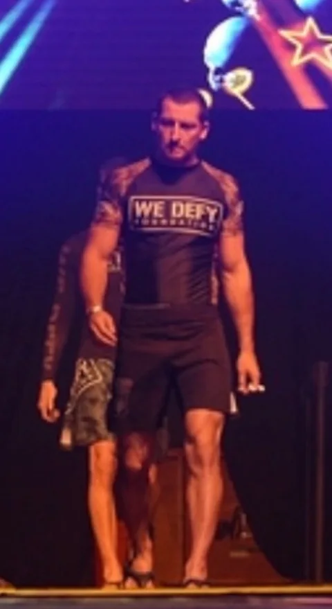 Justin Wood walking out to compete in a We Defy Foundation rash guard and fight shorts.